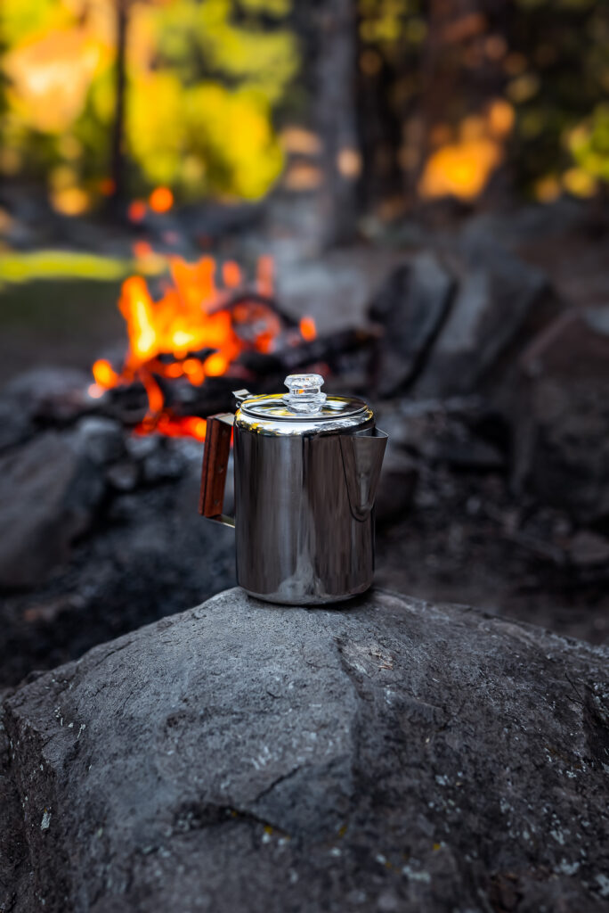 A stainless steel coffee pot on a rock near a campfire, captured by Rex Jones, showcasing outdoor commercial photography in Utah.